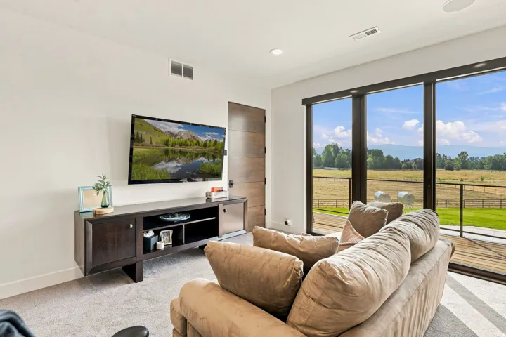 Wall-mounted media console, full-height glass doors, and a deck with metal and glass railing