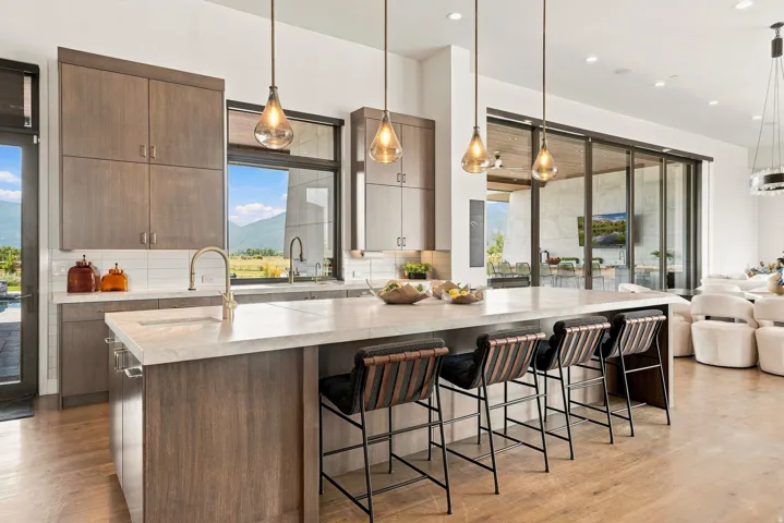 Gourmet kitchen featuring a large island, wood-finish cabinetry, light-toned countertops, pendant lighting, and expansive sliding glass doors