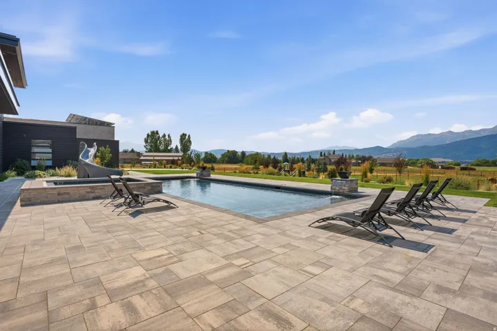Expansive paver patio with an in-ground swimming pool, an adjacent built-in spa, and a built-in water slide