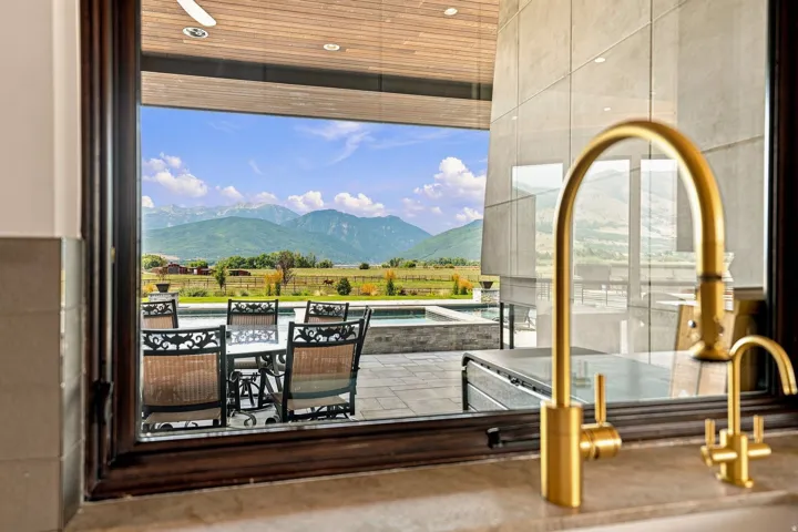 Expansive mountain scenery, outdoor dining area, outdoor pool, modern architecture, and a gold-finish kitchen faucet