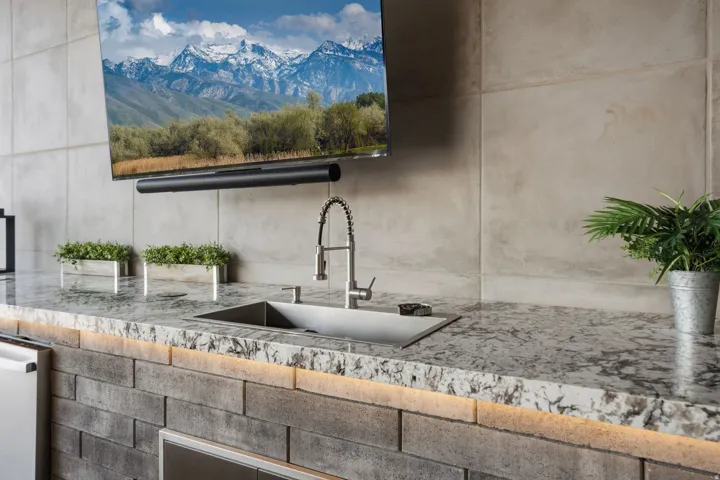 Built-in outdoor kitchen with a stone-finish counter, integrated sink with a gooseneck faucet, and a stone-finish backsplash