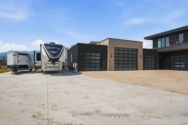 Multiple contemporary garage doors, expansive concrete driveway, stucco exterior finishes, large balcony, and extensive window placement