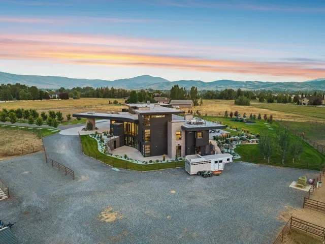 Modern architectural exterior with extensive glass elements, expansive gravel driveway, and surrounding landscaped grounds featuring mature trees and a manicured lawn