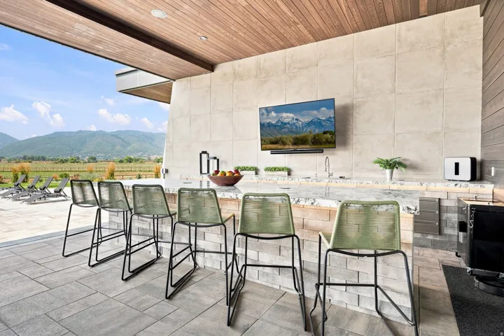 Outdoor living area featuring a wood-finish ceiling, mountain scenery, a built-in bar with a stone counter, a wall-mounted display, and a paver patio