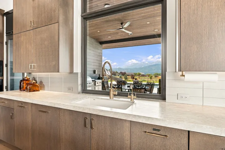 Integrated kitchen sink with a gooseneck faucet, light-toned countertop, wood-finish cabinetry, and a white subway tile backsplash