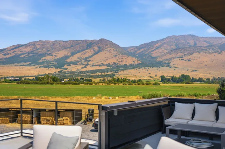 Outdoor deck with dark metal railing, offering expansive views of mountains and green fields