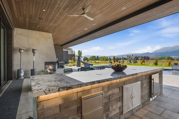 Outdoor kitchen featuring a stone-clad island with integrated appliances and under-cabinet lighting