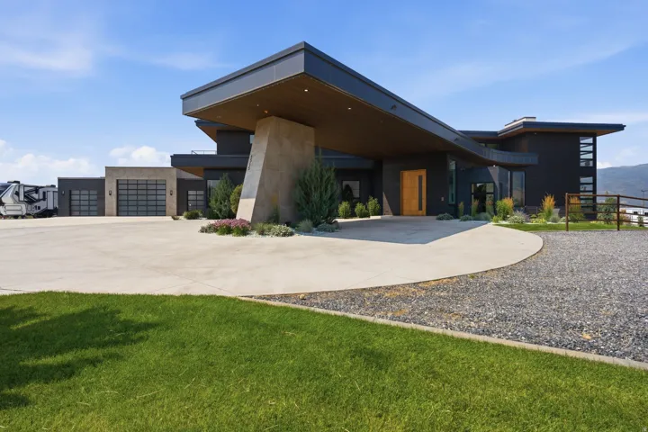 Contemporary exterior with a covered entry, dark facade, and multiple garage doors featuring horizontal glass panels