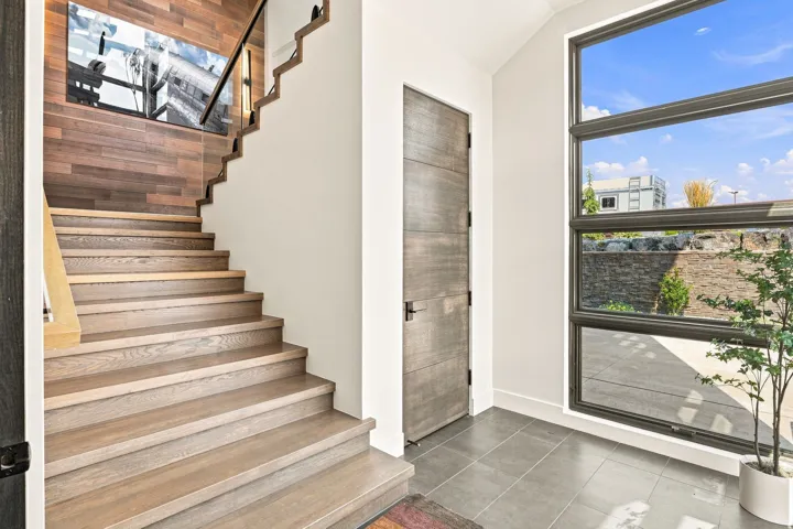 Hardwood staircase with clear panel railing, wood-finish accent wall, and a full-light window