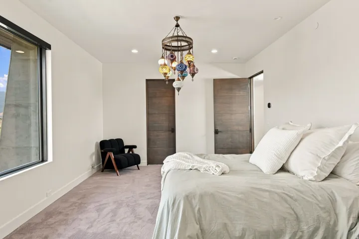 Expansive window with mountain scenery, recessed ceiling lighting, textured gray carpeting, and a unique multi-colored glass chandelier