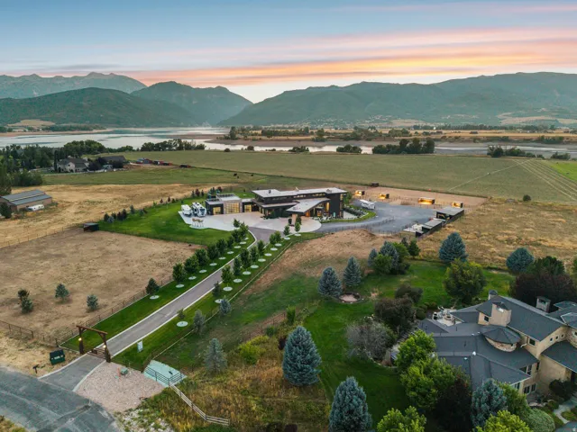 Property featuring a modern architectural residence, extensive paved driveway, established landscaping, and expansive surrounding fields