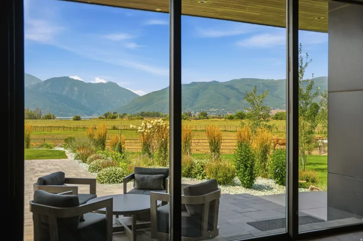 Expansive sliding glass doors, wooden ceiling detail, paver patio, lush landscaping with ornamental grasses, and distant mountain scenery