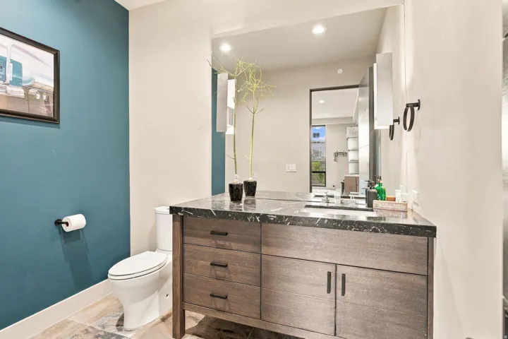 Wood-finish vanity with dark hardware, dark stone countertop, and a basin sink