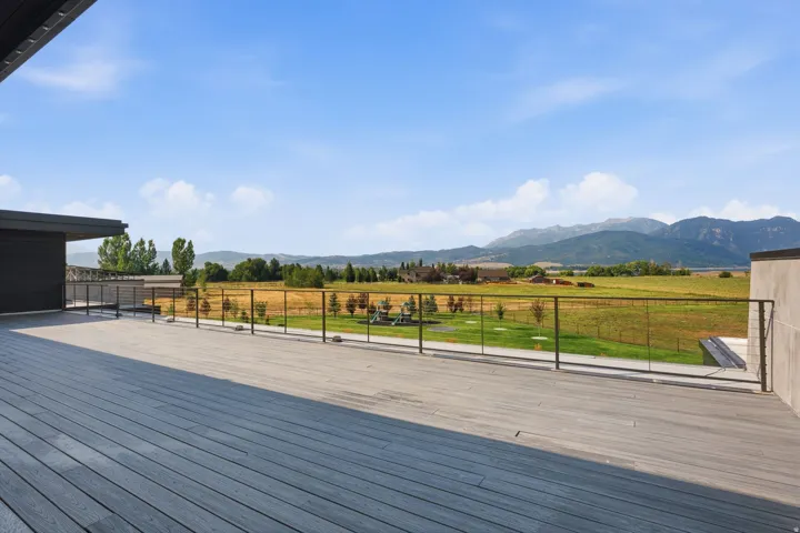 Expansive outdoor deck with composite decking, cable railing, mountain backdrop, and open field scenery