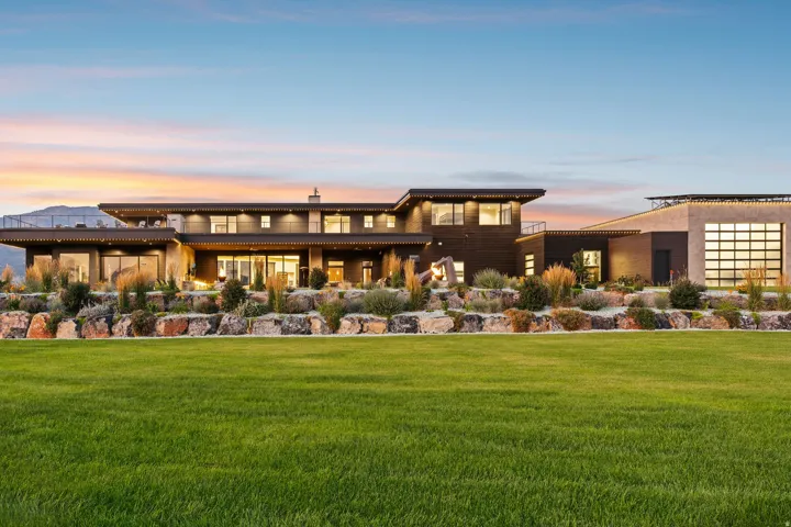 Expansive green lawn with a contemporary multi-level exterior featuring broad eaves, large windows, and an attached structure with a roll-up glass panel door