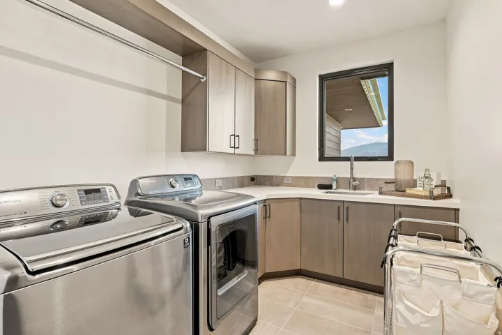 Integrated laundry area with stainless steel appliances, upper and lower cabinetry, a built-in sink, and tile flooring