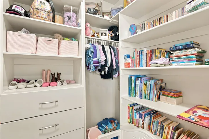 Organized closet space featuring custom white built-in cabinetry with multiple shelves, two lower drawers with metal hardware, and integrated hanging rod