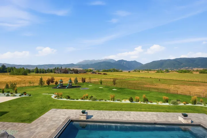 Expansive paver patio with an in-ground swimming pool overlooking a manicured lawn and distant mountain range