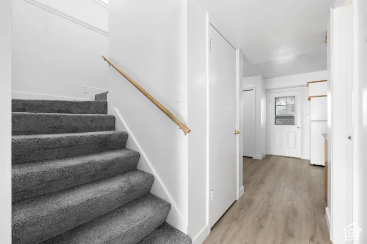 2986 - Carpeted staircase with wood handrail, light wood-finish flooring, white paneled doors, and a white refrigerator