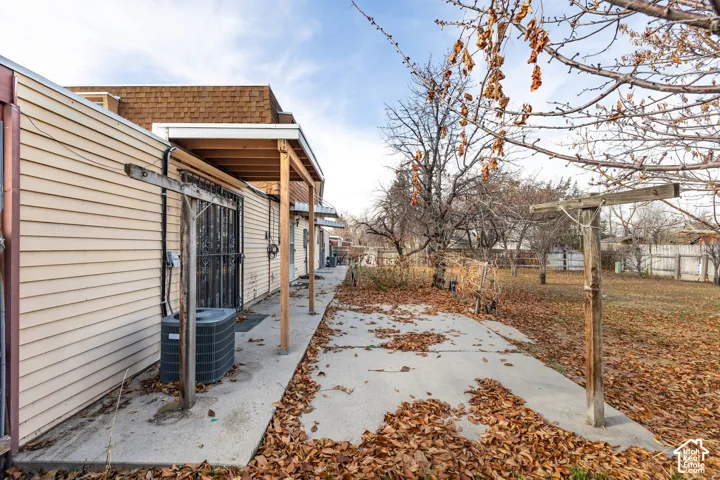 Rear exterior with light-colored siding, concrete walkway, and a wooden patio cover