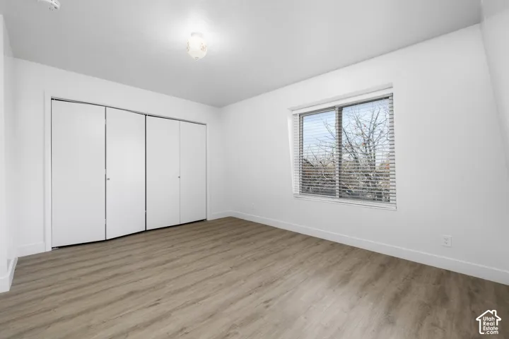2984 - Bright bedroom featuring wood-finish flooring, a large window with blinds, and a spacious closet with sliding glass doors