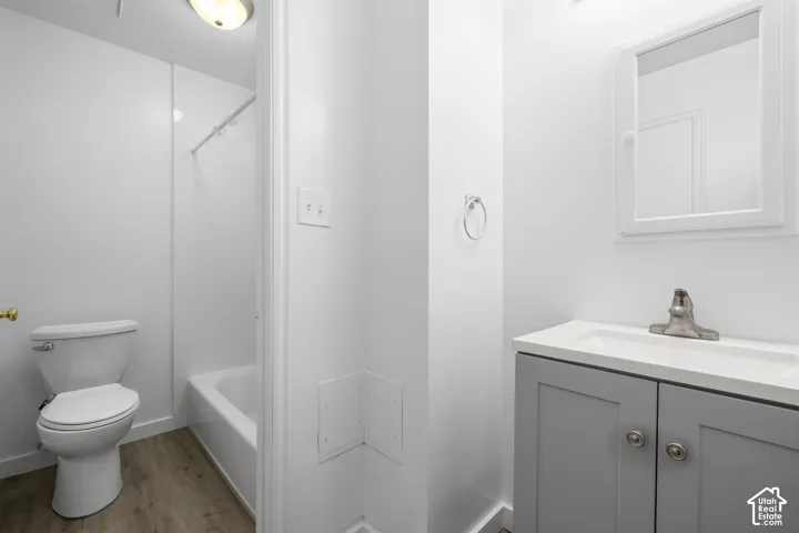 2986 - Bathroom featuring a white toilet, white bathtub with a shower, wood-finish flooring, and a vanity with a white countertop and gray cabinetry