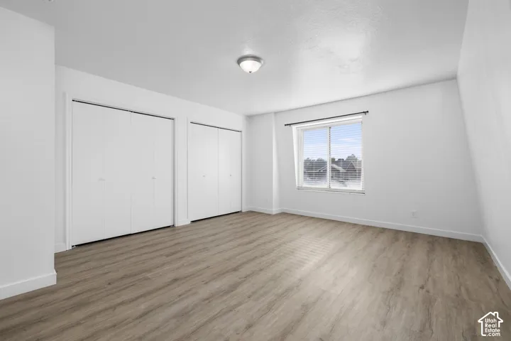 2986 - Spacious bedroom featuring wood-finish flooring, dual closets with sliding doors, large window with natural light, and clean white walls with recessed ceiling lighting