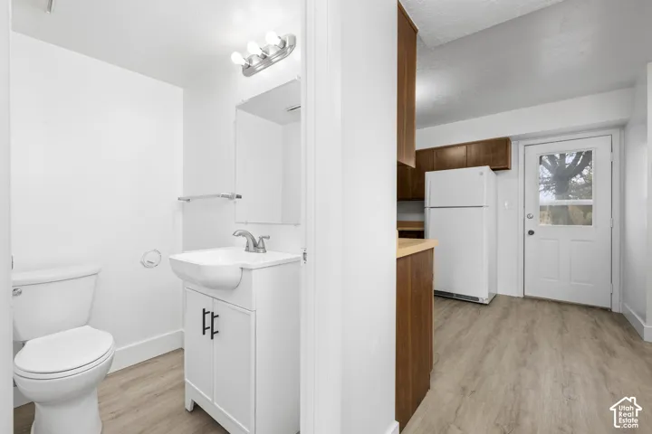 2984 - White toilet, vanity with integrated sink, wood-finish flooring, wood cabinetry, and a white refrigerator