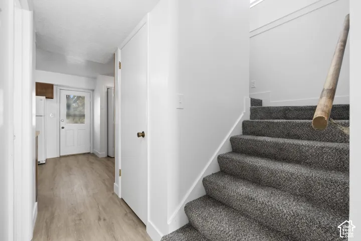 2984 - Gray carpeted staircase with wood railing, leading to a hallway with wood-finish flooring