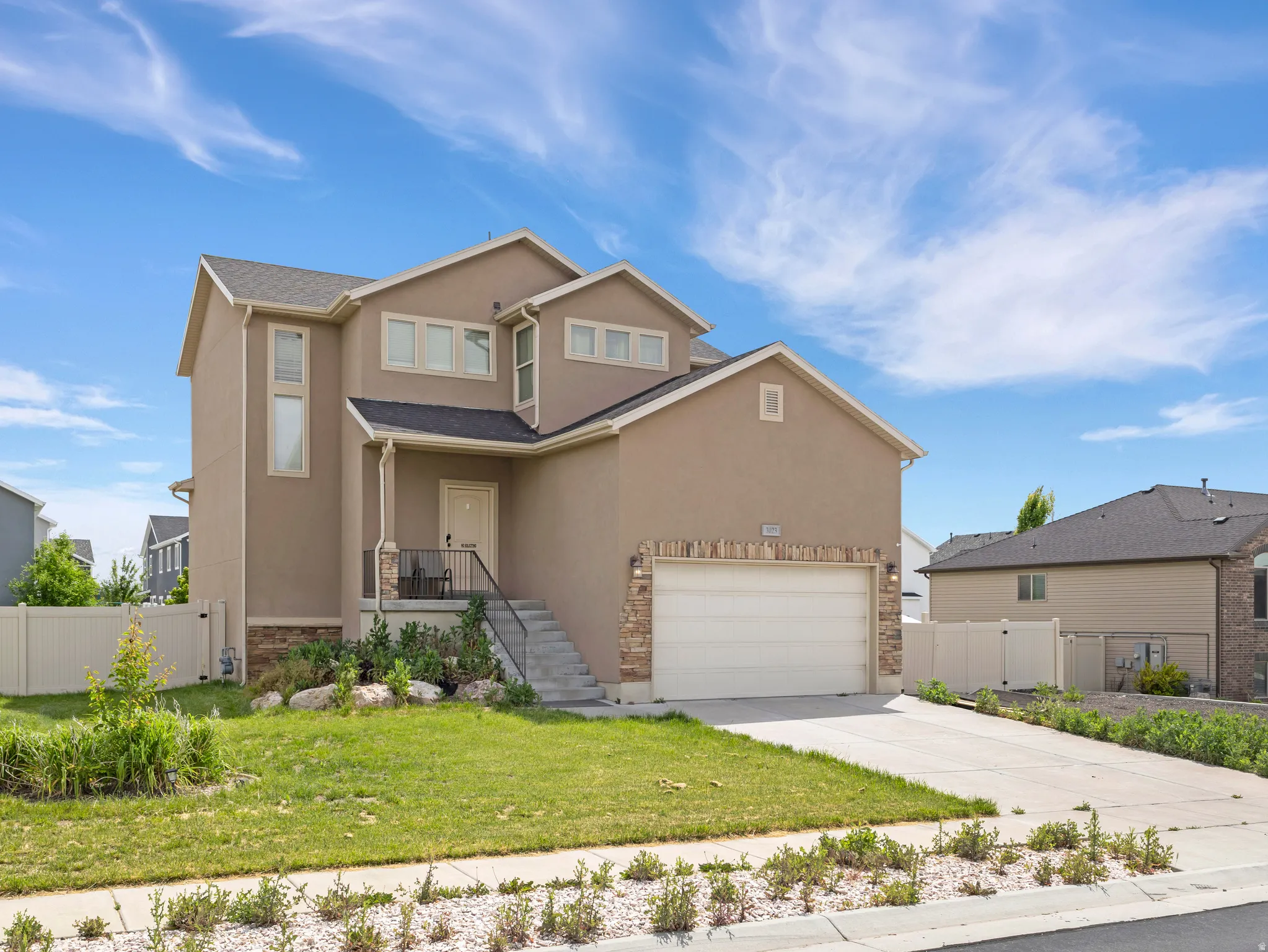 Stucco exterior with stone accent detailing, attached garage, covered porch, and concrete driveway