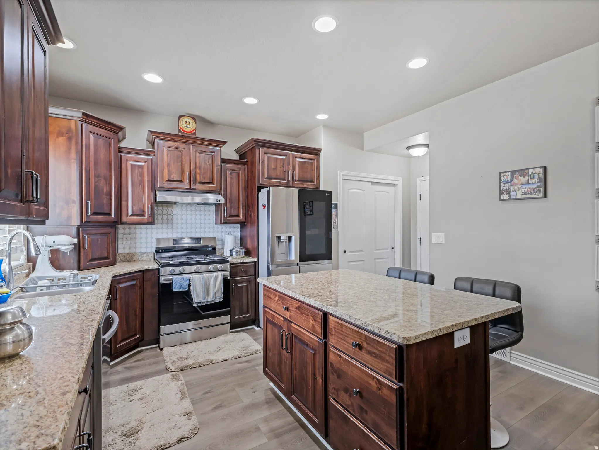 Kitchen featuring dark wood cabinetry, light-toned granite countertops, stainless steel appliances, a tile backsplash, and recessed lighting
