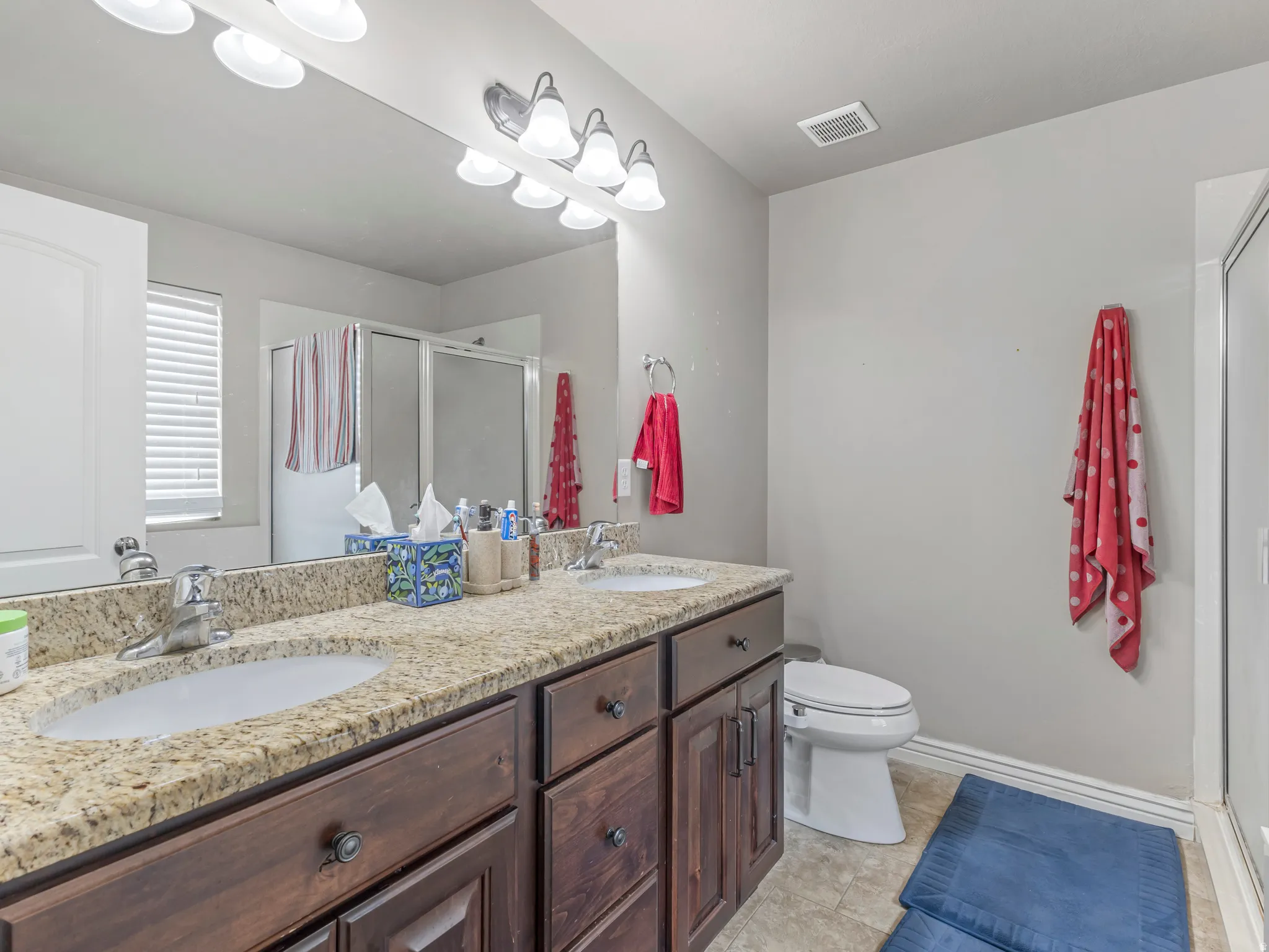 Dual vanity with granite countertop, integrated sinks, wood-finish cabinetry, and overhead lighting