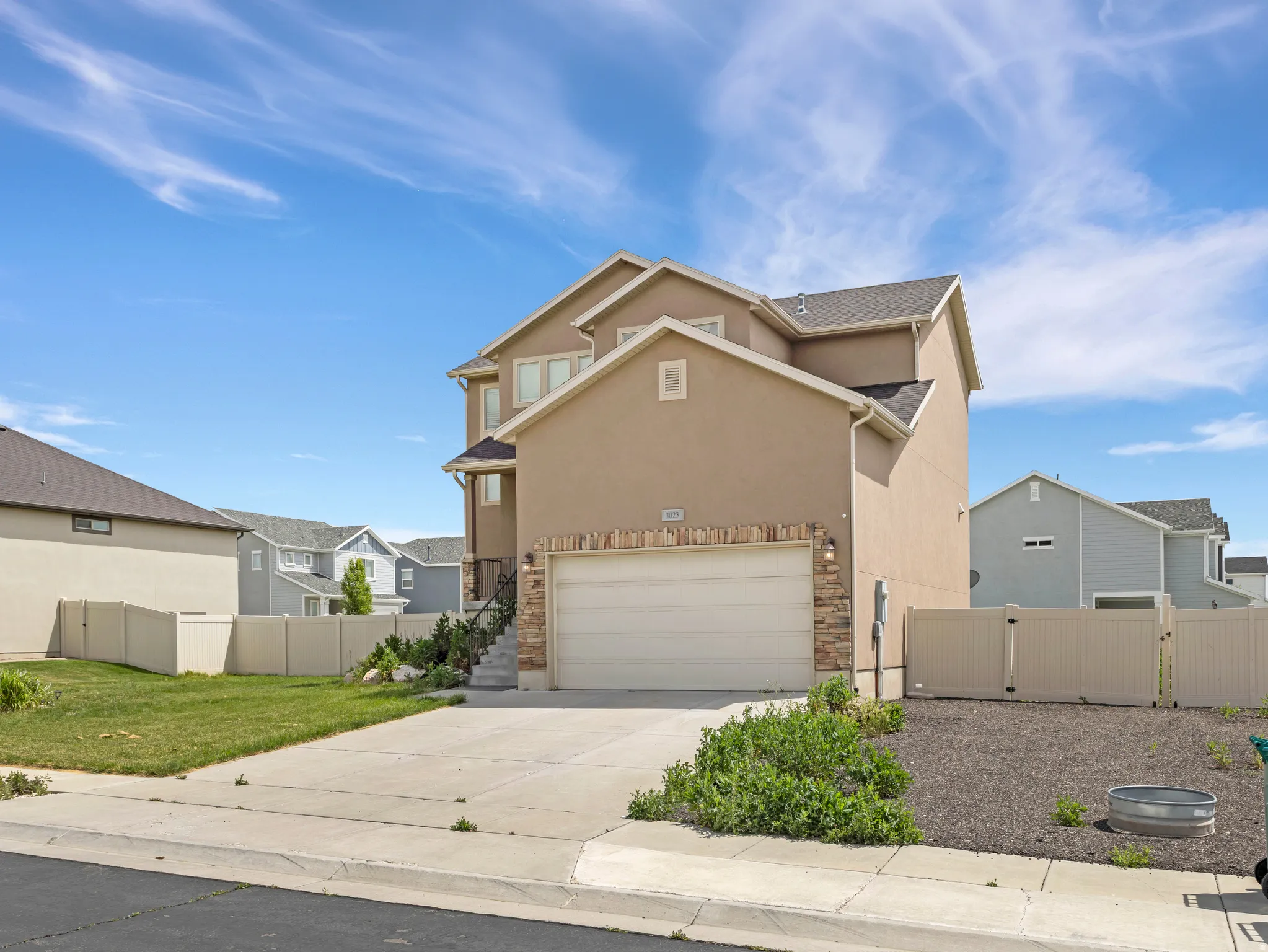 Two-story stucco exterior with stone accents, attached garage, concrete driveway, and privacy fencing