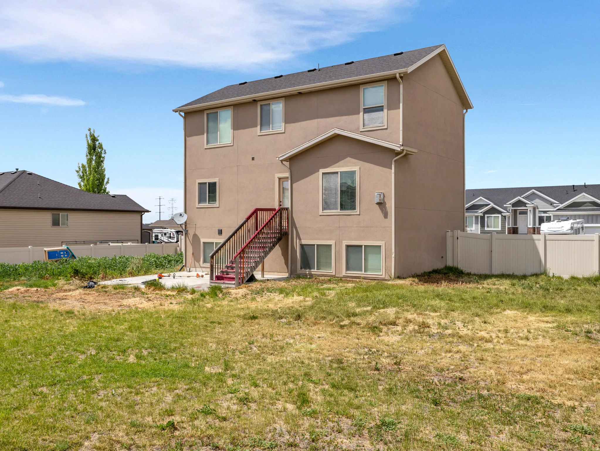 Spacious three-story residence featuring a tan exterior with multiple windows, metal stair railings providing access to the main entrance, and an expansive lawn with mature landscaping