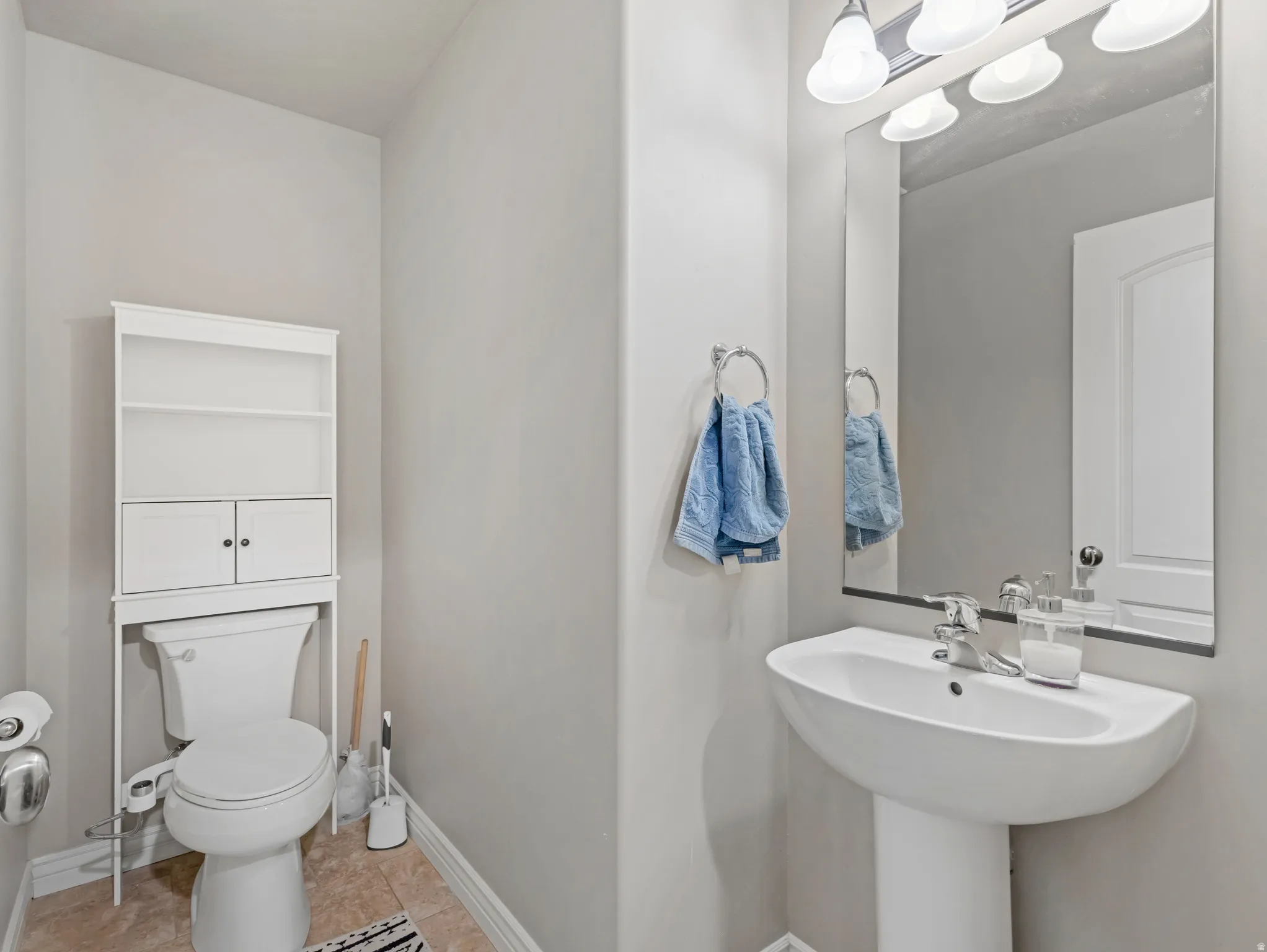 Pedestal sink with chrome faucet, wall-mounted mirror, and vanity lighting fixture