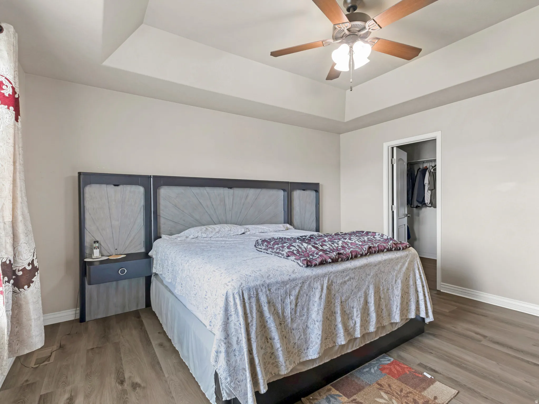 Tray ceiling, wood-finish flooring, ceiling fan with integrated lighting, recessed closet, and neutral wall tones