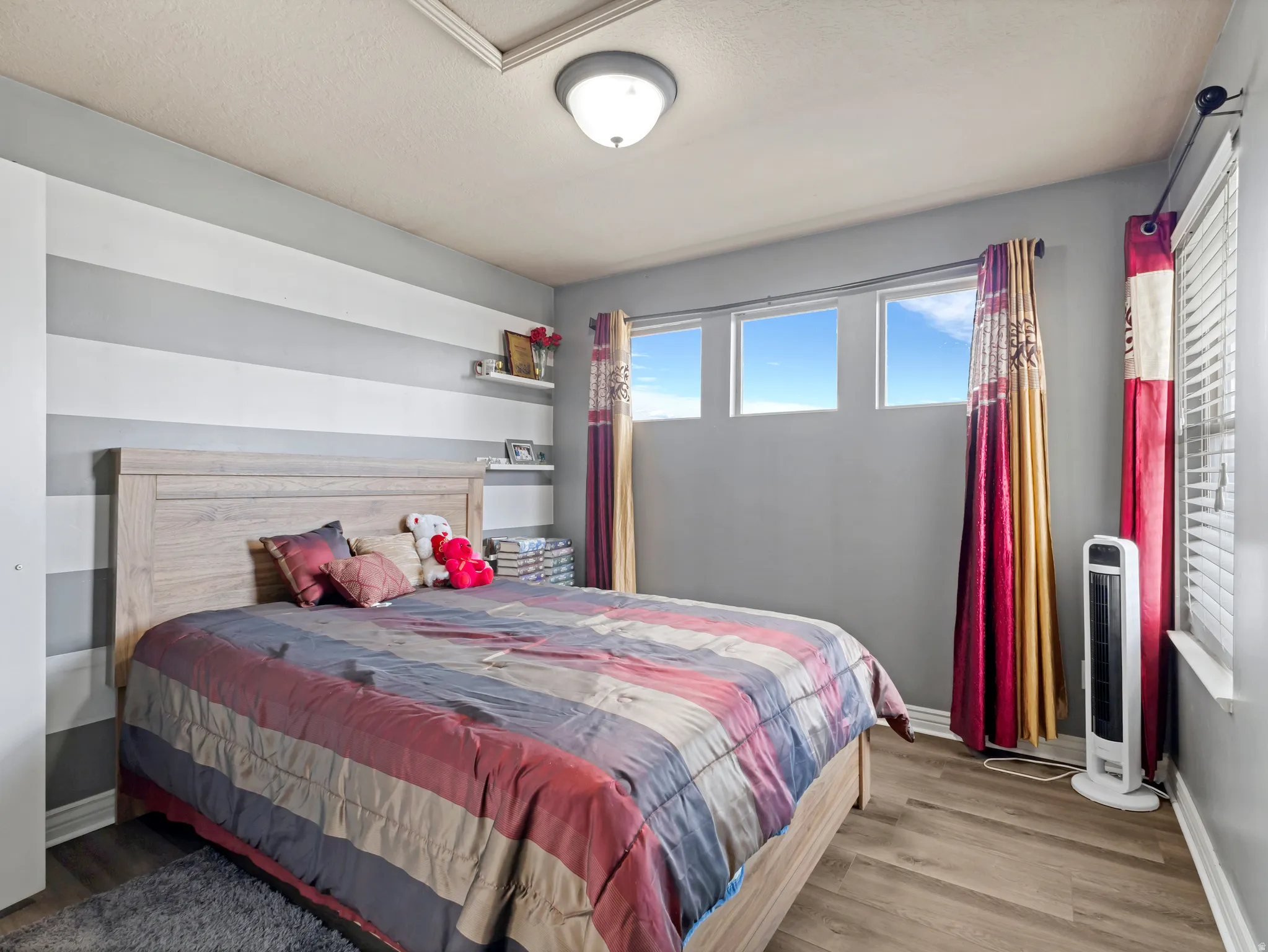 Wood-finish flooring, three transom windows, ceiling-mounted light fixture, and horizontal striped accent wall