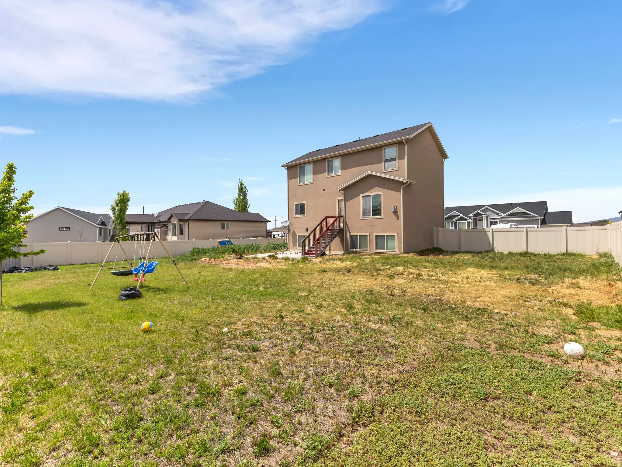 Expansive backyard featuring a two-story residence with a tan exterior, multiple windows, and a privacy fence