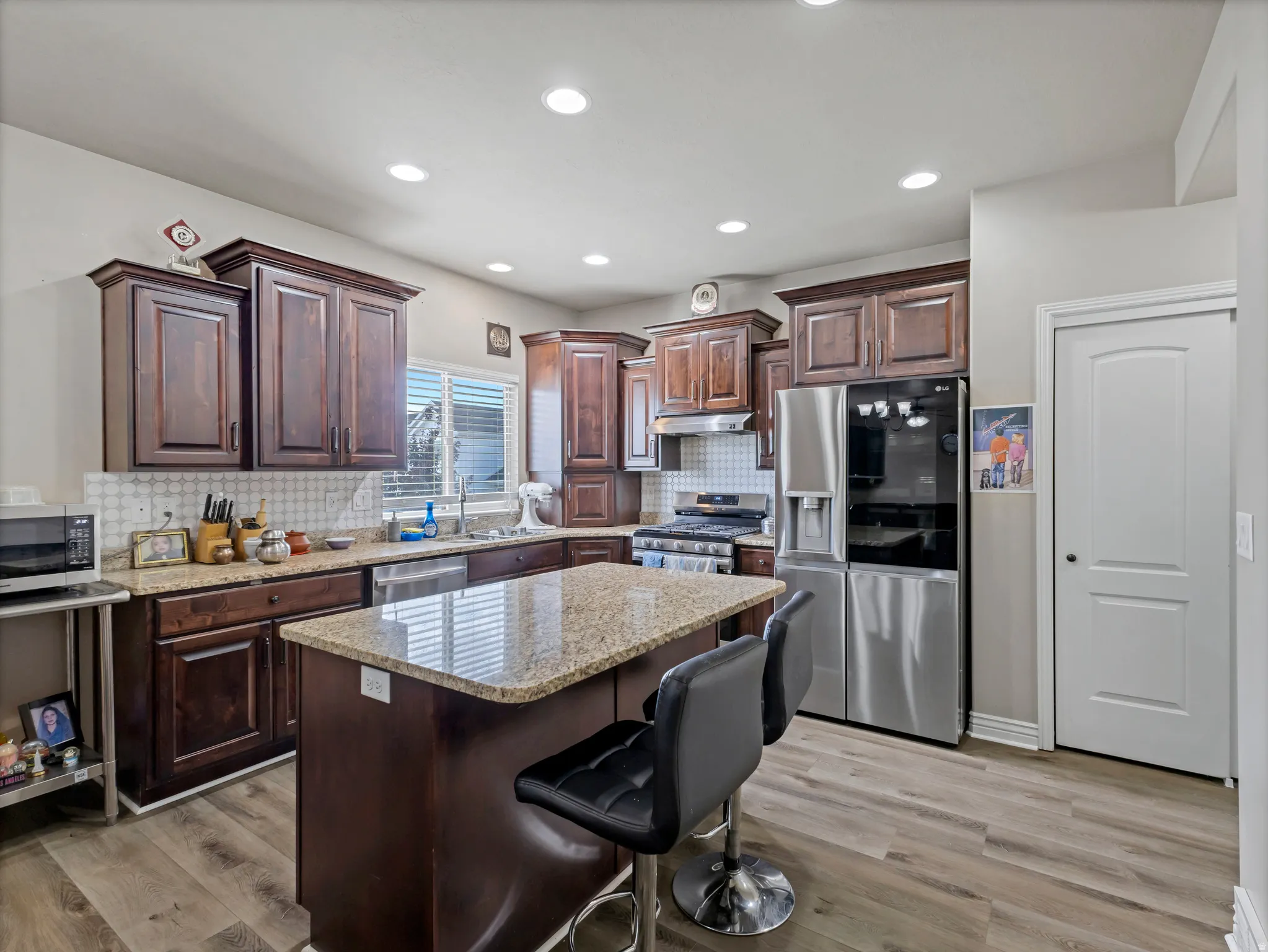 Kitchen featuring dark wood cabinetry, light-toned granite countertops, a center island, stainless steel appliances, and wood-finish flooring