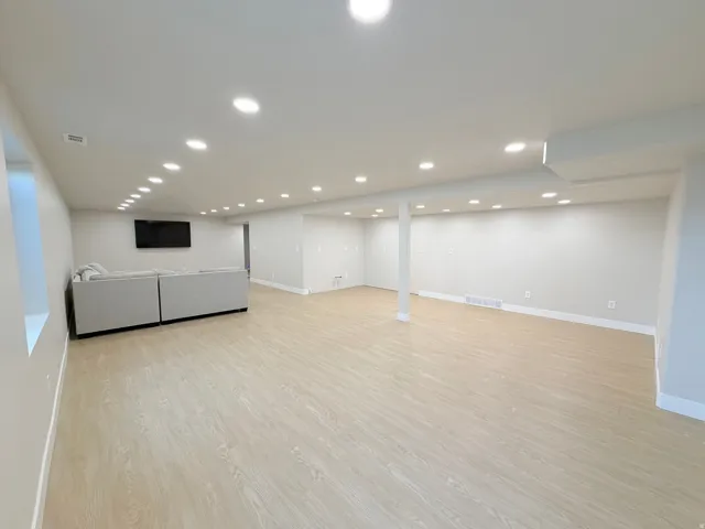 Expansive open-concept room featuring light-toned wood-finish flooring, recessed ceiling lighting, and a neutral wall color