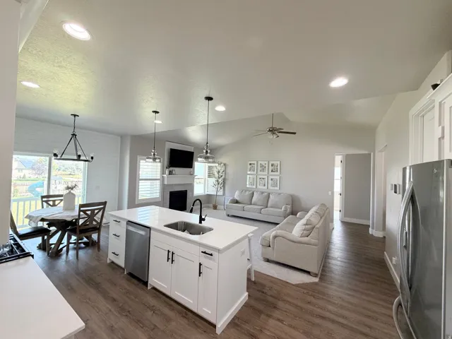 Open-concept living space featuring wood-finish flooring, a kitchen island with seating, recessed lighting, and a fireplace with a mantel