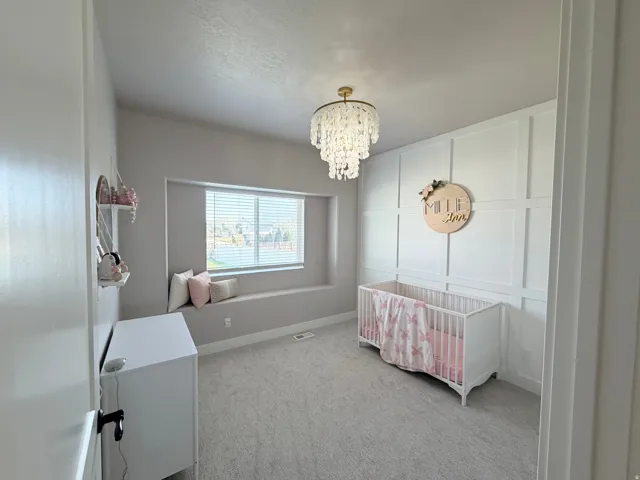 Vaulted ceiling with a crystal chandelier, accent wall with panel molding, window seat with built-in storage, and wall-to-wall carpeting