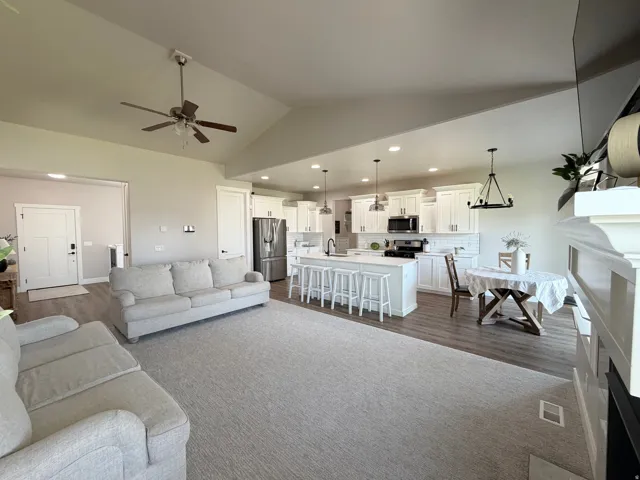 Open-concept living space featuring vaulted ceilings, wood-finish flooring, a white kitchen with an island, and a decorative fireplace