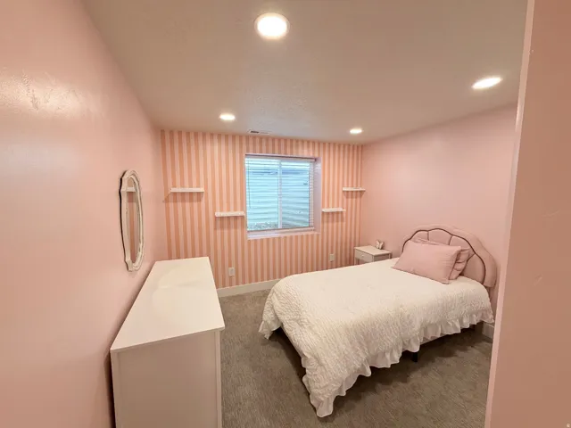 Recessed ceiling lighting, window with blinds, floating wall shelves, soft wall color, and carpeted flooring