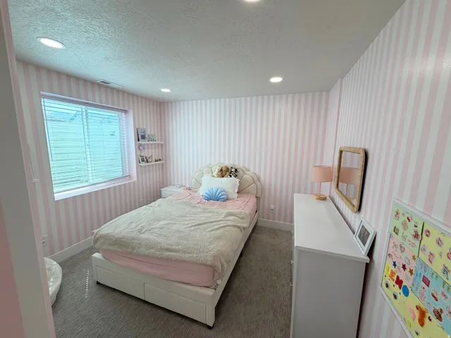 Recessed lighting, patterned wall treatment, wall-mounted shelving, window with horizontal blinds, and carpeted flooring