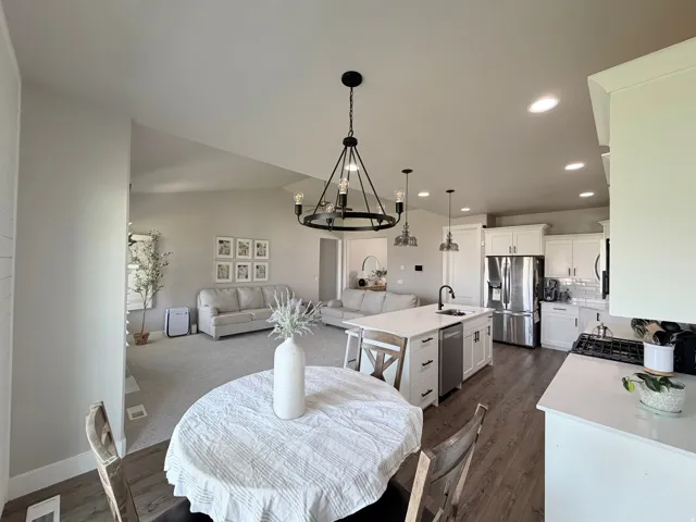 Open-concept living space with vaulted ceilings, wood-finish flooring, a kitchen island with seating, white shaker cabinetry, and stainless steel appliances