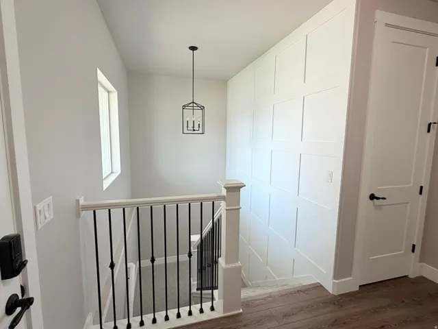Staircase with wood-finish flooring, white paneled accent wall, wrought iron balusters, and a black geometric pendant light