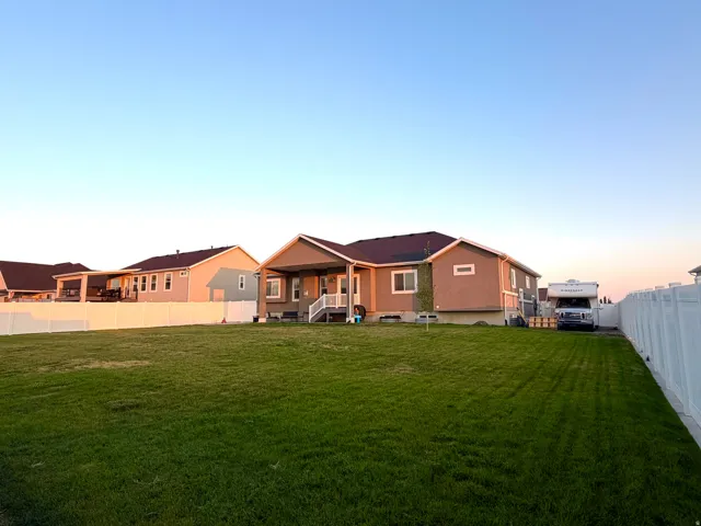 Expansive green lawn, white privacy fencing, covered porch with white railing, and a gravel parking area