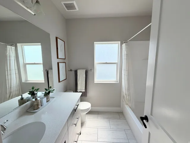 Bathroom featuring a white vanity with an integrated sink, a built-in tub with a shower, and light-toned floor tiles