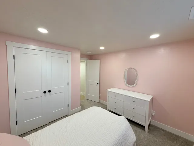 Bright secondary bedroom with soft pink walls, recessed ceiling lighting, and neutral wood-finish flooring